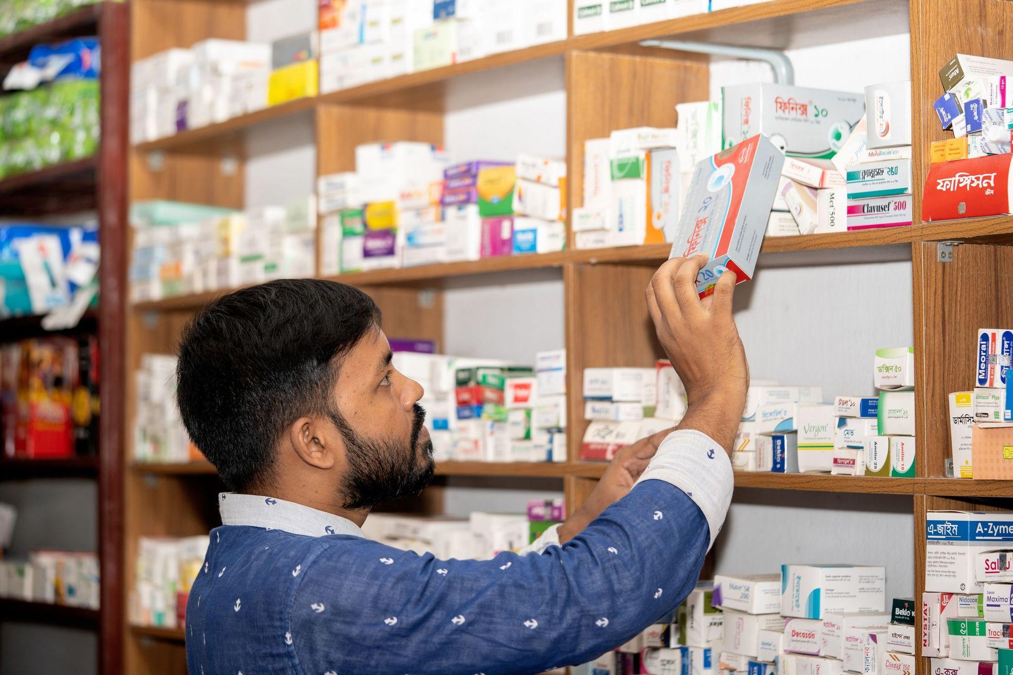 Pharmacien rangeant une boîte de médicament sur les étagères d’une officine.